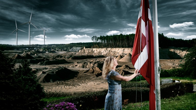 Kvinde der hejser flag og vindmølle i baggrunden