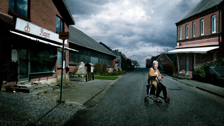 Ældre kvinde der sidder på en rolator på en øde vej