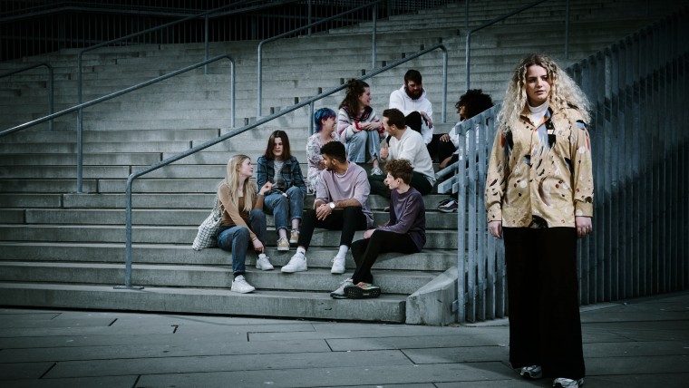 Ung pige der står alene foran en større gruppe unge