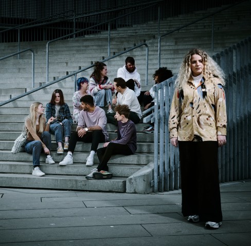 Ung pige der står alene foran en større gruppe unge