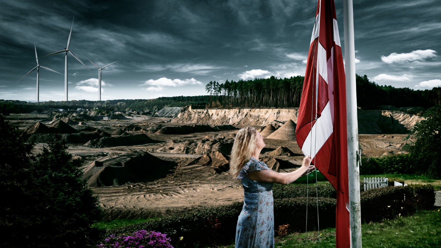 Kvinde der hejser flag og vindmølle i baggrunden
