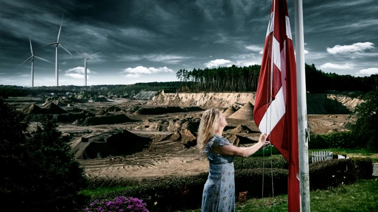 Kvinde der hejser flag og vindmølle i baggrunden