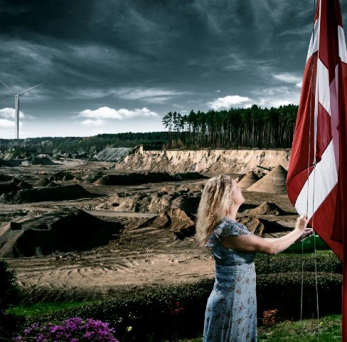 Kvinde der hejser flag og vindmølle i baggrunden
