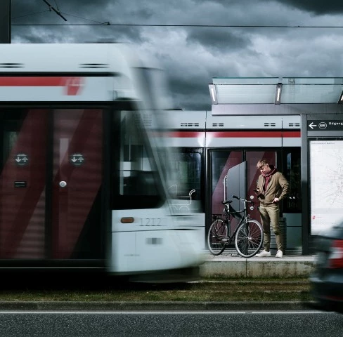 Ung mand på station, hvor letbanen kører forbi