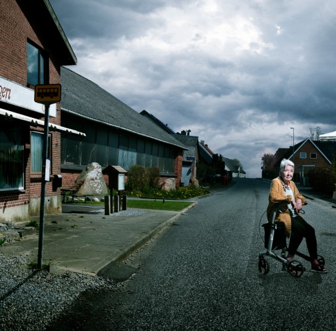 Ældre kvinde der sidder på en rolator på en øde vej